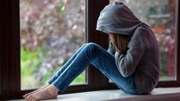 Sad girl in hooded top, sitting on a window ledge with head in hands in despair