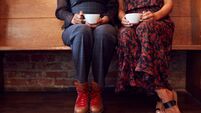 Close Up On Feet Of Female Friends Sitting On Bench In Coffee Shop Together