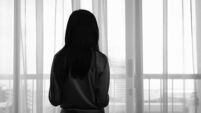 Back view image of sad lonely girl looking trough the window in black and white monochrome photo