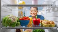 Beautiful Young Woman Looks inside the Fridge and Takes out Vegetables. Woman Preparing Healthy Meal Using Groceries. Point of V