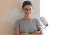 Smiling young woman painting walls in her new house: home renovation and DIY concept