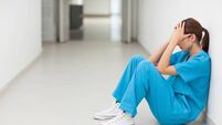 Nurse sitting in a corridor while holding her head