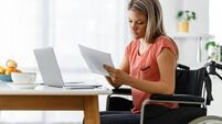 Woman in a wheelchair working on paperwork and laptop at home.