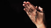 Close-up of a female hand holding rosary beads and a crucifix - John Gollop