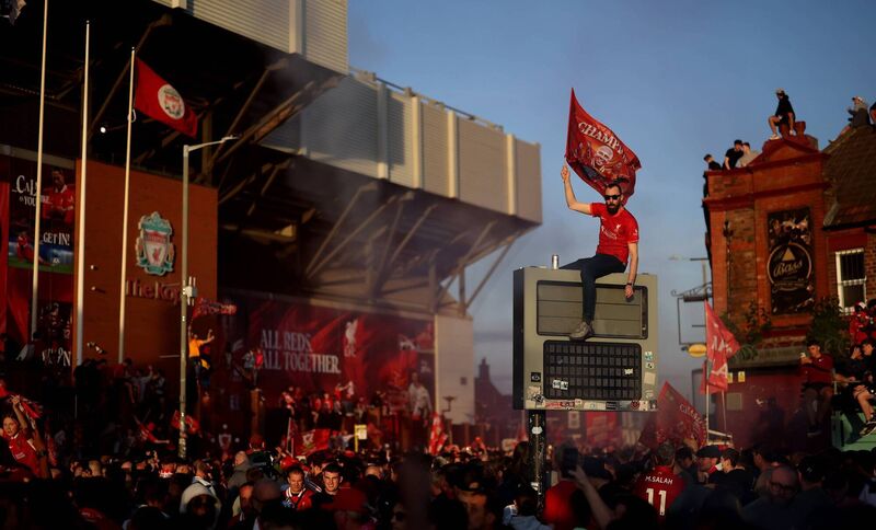 A fan of Liverpool waves a flag, while sitting on top of a sign, as they celebrate the teams victory and confirmation of winning the Premier League title, outside Anfield. Picture: Carl Recine/Getty Images