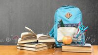 Back to school concept with school books, textbooks, backpack and stationery supplies on classroom desk with teacher's black cha