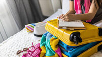 Female hands writing checklist of clothes shoes and accessories packing suitcase to travel vacation