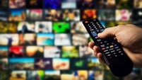 tv channels in background and remote control in hand. smart television and content on demand concept