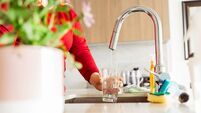 Woman pouring tap water into glass in stylish kitchen in apartment at home, selective focus