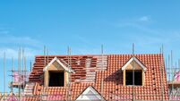 Scaffold poles surrounding the partly tiled roof with dormer windows of a new bungalow being built, against a blue sky.