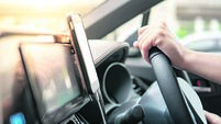 Male driver hand holding on steering wheel using smartphone for GPS navigation. Mobile phone mounting with magnet on the car con