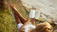 Woman lying in a hammock on the beach and enjoying a book reading