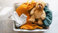 A laundry basket with dirty laundry and a teddy bear