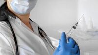 Nurse pushing air out of syringe for vaccine injection. Doctor wearing blue gloves and medical mask. Person holds a syringe with