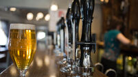 A pint of lager in a pub with a member of staff behind the bar