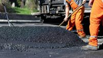 Workers laying asphalt on a road construction site during daylight hours, focusing on creating a smooth surface for vehicles