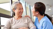 friendly caregiver of nursing home talking to asian senior woman in hallway