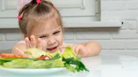 a little girl emotionally pushes away a plate of offered vegetables. children refuse vegetables in favor of junk food