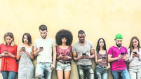 Multiracial friends using smartphone against wall at university college backyard - Young people addicted by mobile smart phone -
