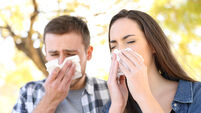 Sick couple sneezing together covering mouth with wipes in a park