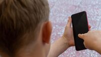 Young boy sitting outside holding a mobile or cellular smart phone. Connectivity, internet, millenial, screen time concepts.