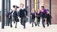 Primary school kids, wearing school uniforms and backpacks, running on a walkway outside their school building, front view
