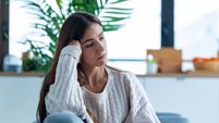 Depressed young woman thinking about her problems while sitting on the sofa at home.