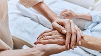 Relative holding trembling hand of senior woman with Parkinson's disease lying in hospital bed at medical ward. Diagnosis and tr