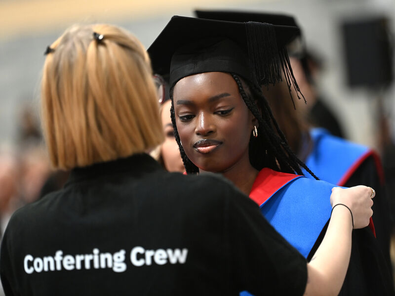  A member of the conferring crew adjusts the gown of graduate Ida Drammeh (BA in Early Childhood Education and Care).