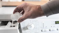 person using dosing aid to fill fabric softener into washing machine