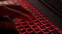 Close up of fingers typing on glowing red backlight keys on a computer keyboard. in the dark. Computer hacker, internet fraud or