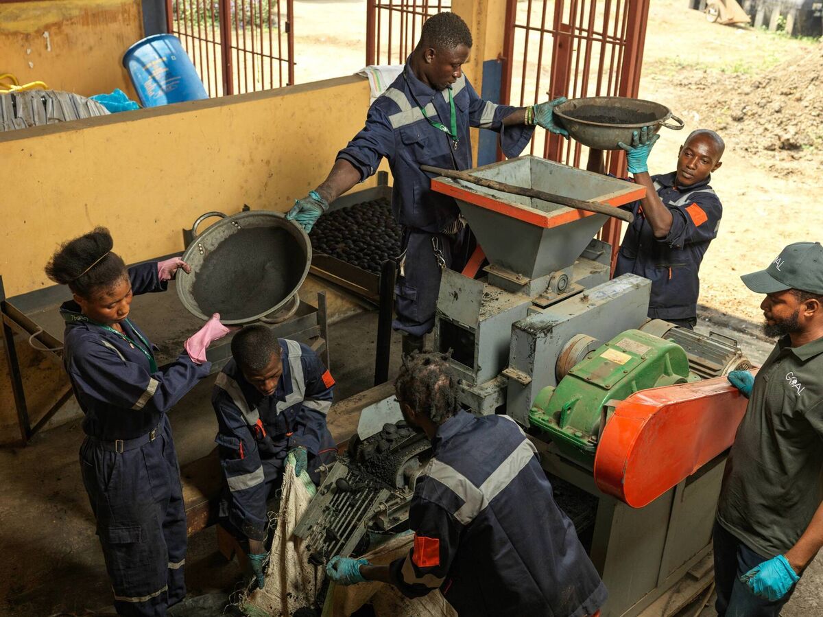 Shaping the future: Workers carefully add the prepared mix into the briquette-forming machine. It is pressed and shaped, ready for use. Photograph: Peter Caton for GOAL Global
