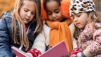 Three small girls reading a children's book in autumn day.