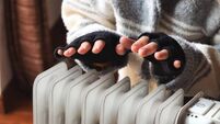 Person heating their hands at home over a domestic portable radiator in winter