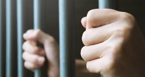 Man in prison hands of behind hold Steel cage jail bars. offender criminal locked in jail.